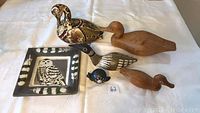 All items displayed: decorative wooden duck decoy, two natural wood duck decoys, ceramic owl tile, black stoneware loon figurine