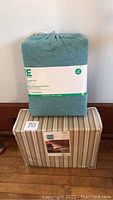 Photo of teal queen size sheet set in original packaging placed on top of twin size striped sheet set box.