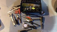 Top view of small black toolbox open showing various hand tools and hardware items inside and around it on the floor.