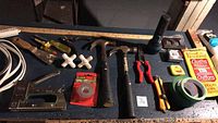 Wide shot showing all the tools and supplies arranged on a table including staple guns, hammers, screwdriver, tape, wire, and others.
