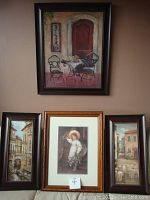 Four framed art prints displayed on a wall showing the medium-size bistro scene art print and three smaller prints depicting European canal street scenes and a girl with flowers.