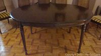 Oval wooden dining table with four turned legs in dark wood finish, visible surface wear and marks.
