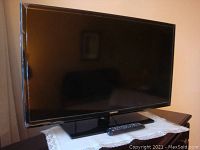 Full view of Samsung TV on stand with remote control on a lace doily.