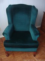 Front view of the green velour wingback armchair, showing plush seat cushion, padded arms, and high wingback design.