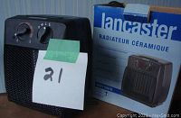 Photo of the black Lancaster ceramic heater alongside its original retail box labeled Lancaster Radiateur Ceramique, showing the heater and its control dials.