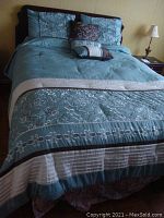 Full view of bed made with teal comforter showing floral embroidery, striped accents, and coordinating pillows.
