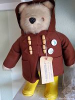 Front view of the Paddington bear showing face, coat with toggles, pins, travel tag, and yellow boots.