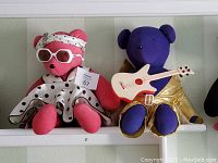Pair of V.I.B. Vintage bears displayed on a shelf - Marilyn Bearoe pink bear wearing white polka dot dress and sunglasses; Elvis Bearsley purple bear dressed in gold lame suit holding guitar.