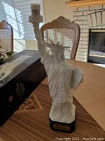 Porcelain Statue of Liberty figurine in white standing on black base, torch raised, on dining table near its original box.