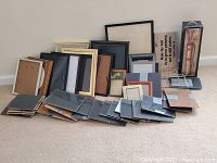 Photo of 50 picture frames in various sizes, some with black, wood-tone, and metallic frames, arranged against a wall.