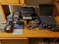 Complete lot arranged on a wooden surface showing laptop, camcorder, Zip drive with disks, various cables, and carrying cases.