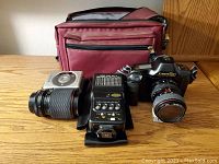 Canon T90 camera with zoom lens, flash unit, and burgundy carry case lined up on wood surface for overview of main items in lot.