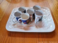 Top view of white Italian ceramic Christmas serving dish with six ceramic holiday coffee mugs placed inside.