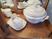 Sugar bowl with lid, creamer and matching underplate alongside footed soup tureen in display cabinet
