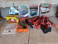 Overview of classic car stands, repair tools, magazines, and parts guide spread on floor.