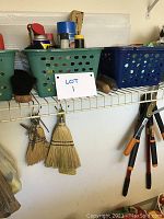 Shelves with plastic bins containing assorted small supplies, hanging brooms and hand tools below