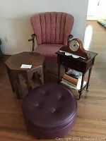 Rose antique accent chair and small wooden hexagonal table, burgundy leather tufted round ottoman, and wooden mantel clock on side table with books beneath.
