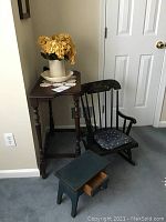 Photo showing child's wooden rocking chair with floral cushion, small wooden side table with turned legs, and painted step stool with drawer.