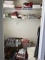 Photo showing wire shelving with folded light colored linens, throws and blankets, bags stored below, and hangers hanging on rod