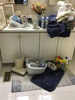 View of towels and bath mats, foot massager, cleaning supplies on and around a white cabinet