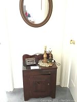 Small dark wood antique cabinet with drawer and door, two table lamps on top, indoor setting.