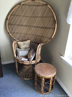 Wicker peacock chair and matching stool placed in a corner near a window, with visible decorative pillows on the chair.