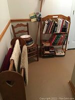 Photo showing a corner with a wooden ladder back chair holding a stack of ceramic serving bowls, a bookshelf filled with books, and a wooden quilt rack leaning against the wall.