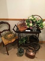 Antique tea/bar cart with antiques and decor including chair, baskets with artificial flowers, copper kettle and metal decorative items.