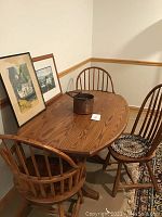 Overall view of the oak oval table with three spindle-back chairs arranged around it.