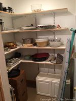 Corner pantry shelves with various kitchen items including glass bowls, metal trays, electric griddle, ceramic bowls, and plastic containers. Also visible are a filing cabinet, iron, ironing board, and two chairs.