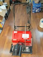 Front view of red Craftsman electric snow blower on wooden floor, showing handlebars, and power switch area.