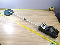 Full view of the Micronta metal detector showing the long shaft and round detection coil with measuring tape showing approx. 38 inch length.