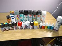 Overview photo of various modeling supplies including spray cans, small jars, and bottles arranged on a table.