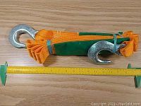 Folded orange towing strap with metal hooks on each end, laid beside a ruler showing approximately 13 feet length when unfolded.