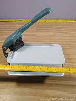 Lassco Wizer Cornerounder paper punch showing entire lever and base surface against measuring tape for scale.