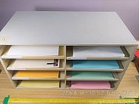Front view of grey metal stationary organizer showing paper samples on shelves