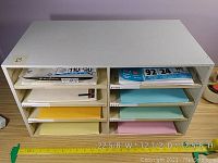 Front view of white stationary organizer with shelves containing colored paper samples, with measurement tape showing width 22 5/8 inches.