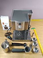 Full lot view showing machine, steam wand, portafilter, handle, frothing pitcher, baskets, tamper, scoop and coffee bag