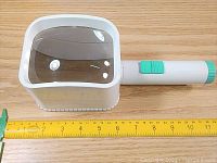 Front view of the bulky square lens magnifier with handle and LED on/off slider switch next to yellow ruler for size reference.
