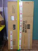 Full view of the unopened cardboard box labeled Technics SH-KS37 color Black with tape and a measuring tape alongside showing height.