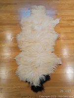 Top view of white sheep skin rug with fluffy long wool and black marking on one end, showing overall size and texture.