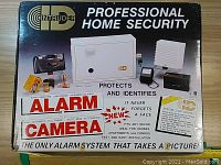 Box front showing product branding, product components, and features including integrated 35mm camera and infrared alarm.