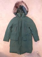 Full view of men's green Arctic style parka with hood and fur trim, showing front pockets and overall length.