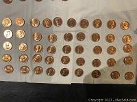 Obverse side of many 1964 one cent coins laid out on fabric, showing Abraham Lincoln portrait close-up.