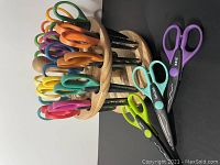 Photo shows 17 colorful Kraft Edgers craft scissors in wooden rotating carousel, with 3 scissors removed and laid next to stand showing different blade edge patterns.
