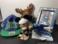 Lot including Vancouver Canucks baseball cap, plush moose toy, framed Roberto Luongo hockey card, McFarlane action figure of Roberto Luongo, and Mickey Mouse bobblehead dressed as hockey player.