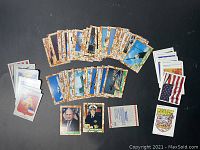 Overview photo of 61 Desert Storm trading cards and 22 stickers spread on black background showing front of cards and stickers, including cards featuring military aircraft and portraits.