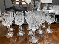 Photo showing 11 clear crystal stemmed wine glasses arranged on a wooden table, highlighting the cut and etched patterns on the bowls.