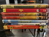 Photo of 7 Disney DVDs stacked horizontally. Titles include Shrek Forever After, Kung Fu Panda series, and Shrek series DVDs.