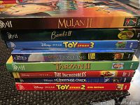 Photo showing a stack of 8 Disney DVDs including Mulan II, Bambi II, Toy Story 3, Lion King 1½, Tarzan II, The Incredibles, A Christmas Carol, and Toy Story 2 DVD Edition.